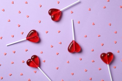 Sweet heart shaped lollipops and sprinkles on violet background, flat lay. Valentine's day celebration