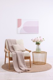 Comfortable armchair with blanket, pillow, table and beautiful flowers in room