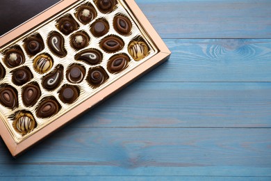 Box of delicious chocolate candies on light blue wooden table, top view. Space for text