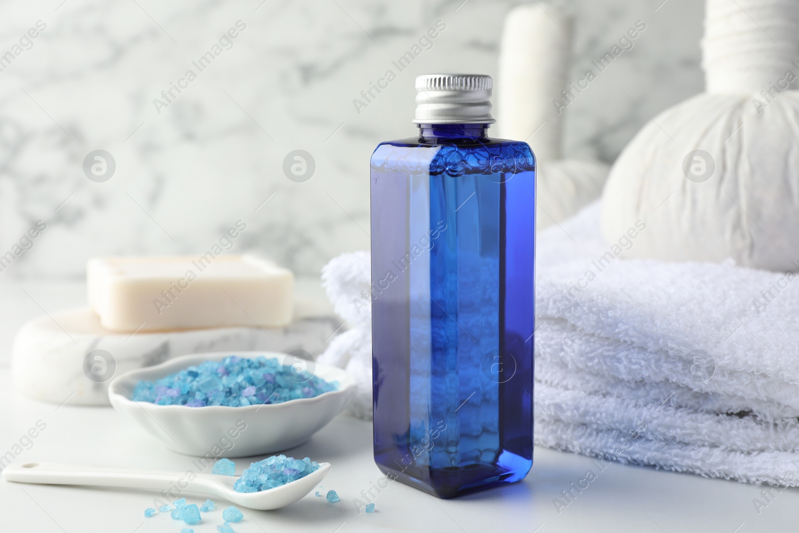 Photo of Spa composition. Bottle of cosmetic product, sea salt, towel, soap and herbal bags on white table