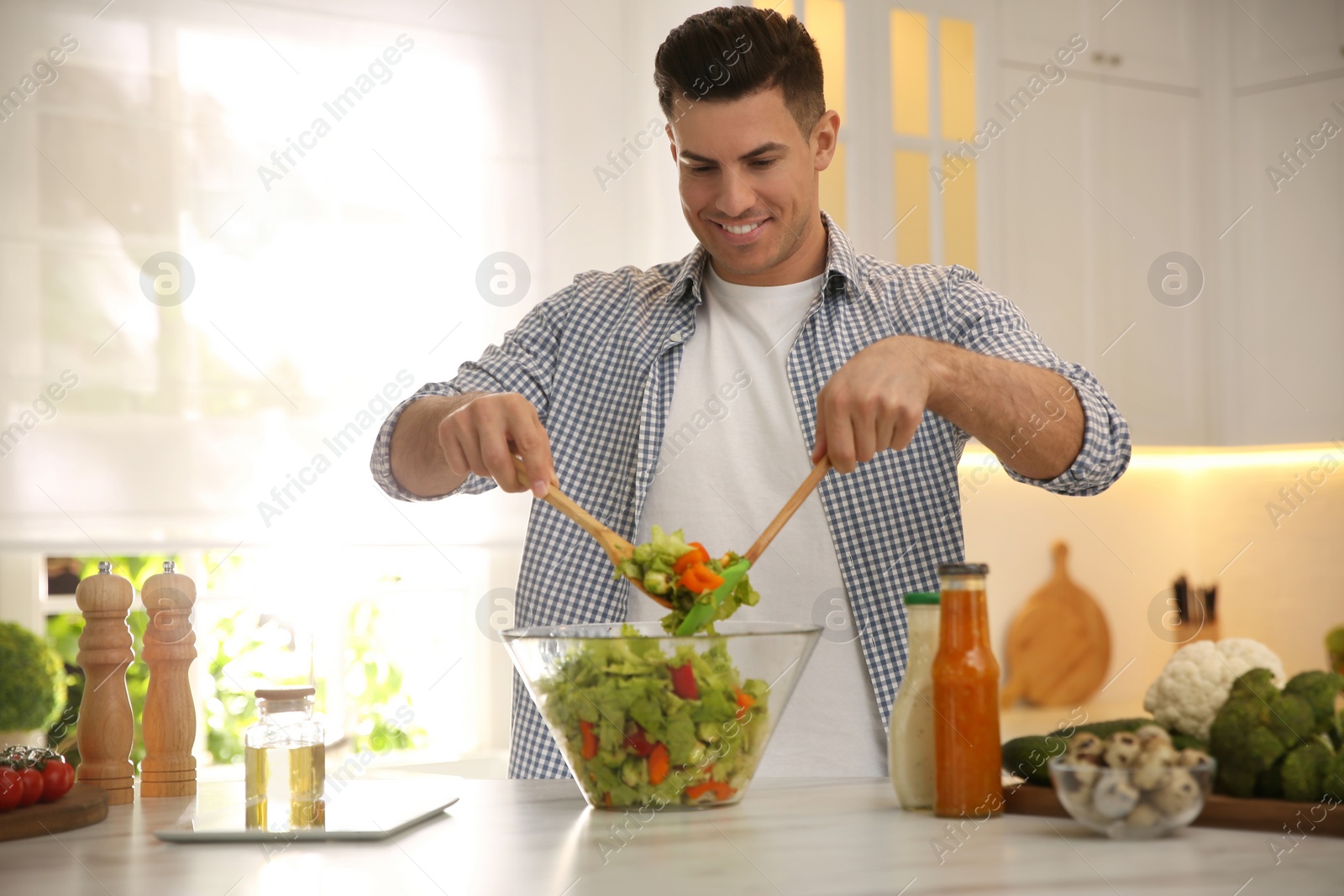 Photo of Man with tablet cooking salad at table in kitchen