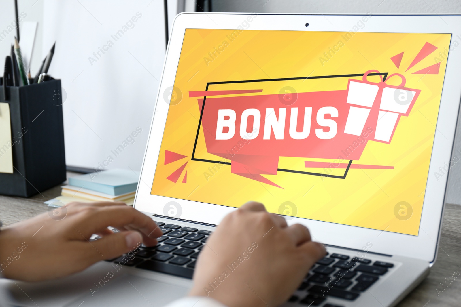 Image of Bonus gaining. Woman using laptop at table, closeup. Illustration of gift box and word on device screen