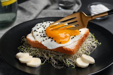 Photo of Tasty toast served with egg, cheese and microgreens on black plate, closeup