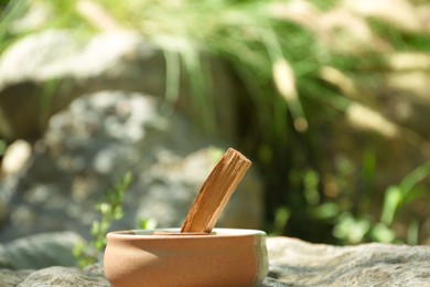 Photo of Palo santo stick in holder on stone outdoors. Space for text