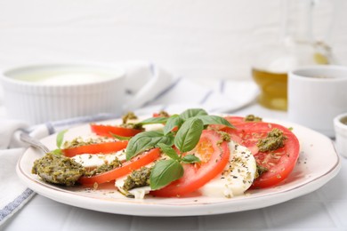 Photo of Plate of delicious Caprese salad with pesto sauce on white tiled table, closeup
