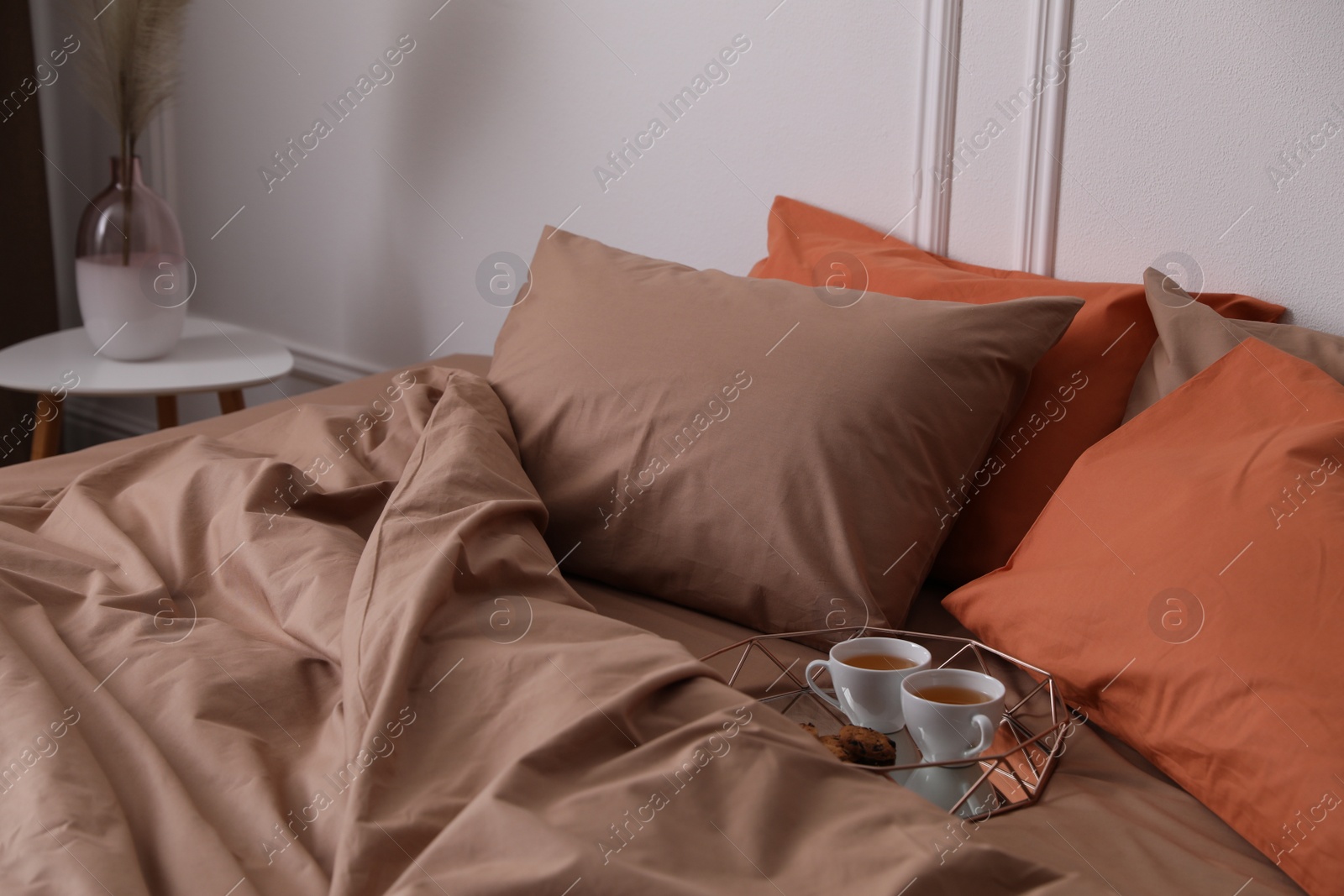 Photo of Cups of hot drink and cookies on bed with brown linens in stylish room