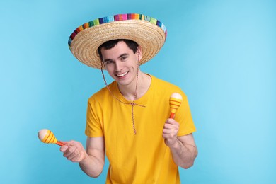 Photo of Young man in Mexican sombrero hat with maracas on light blue background