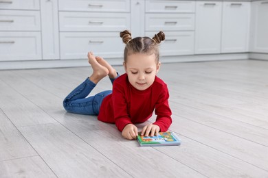 Photo of Cute little girl reading book on warm floor in kitchen. Heating system