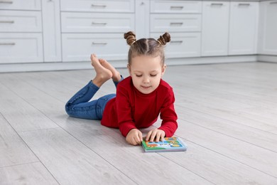 Cute little girl reading book on warm floor in kitchen. Heating system