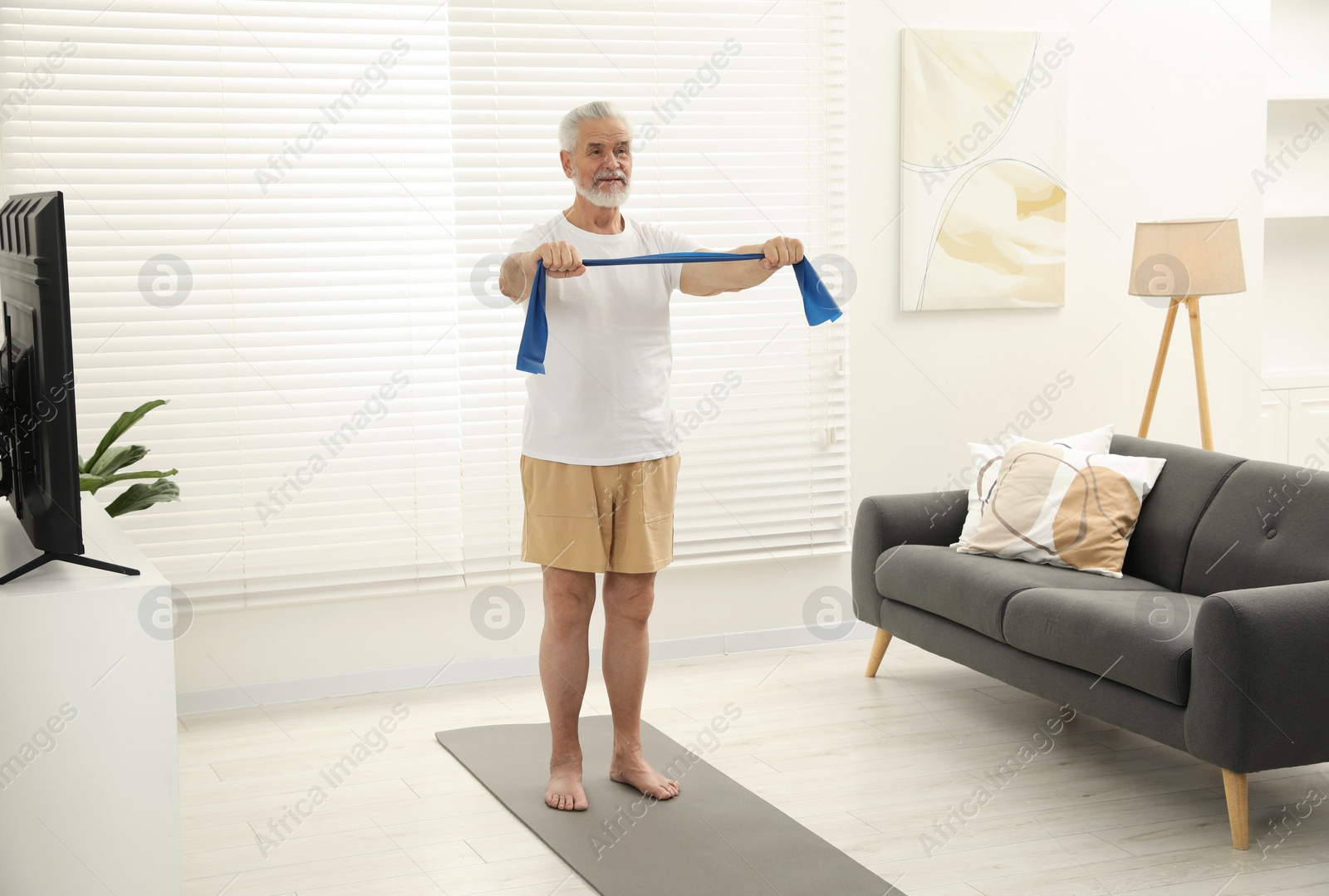 Photo of Senior man doing exercise with fitness elastic band on mat at home