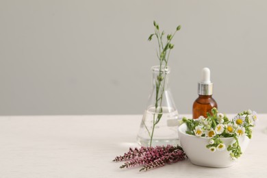 Photo of Bottle of cosmetic oil and flowers on white table, space for text