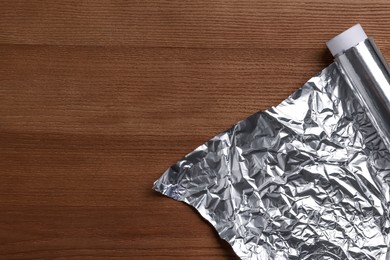 Photo of Roll of aluminum foil on wooden table, top view. Space for text