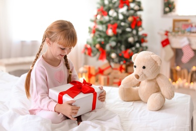 Cute little child with Christmas gift box sitting on bed at home