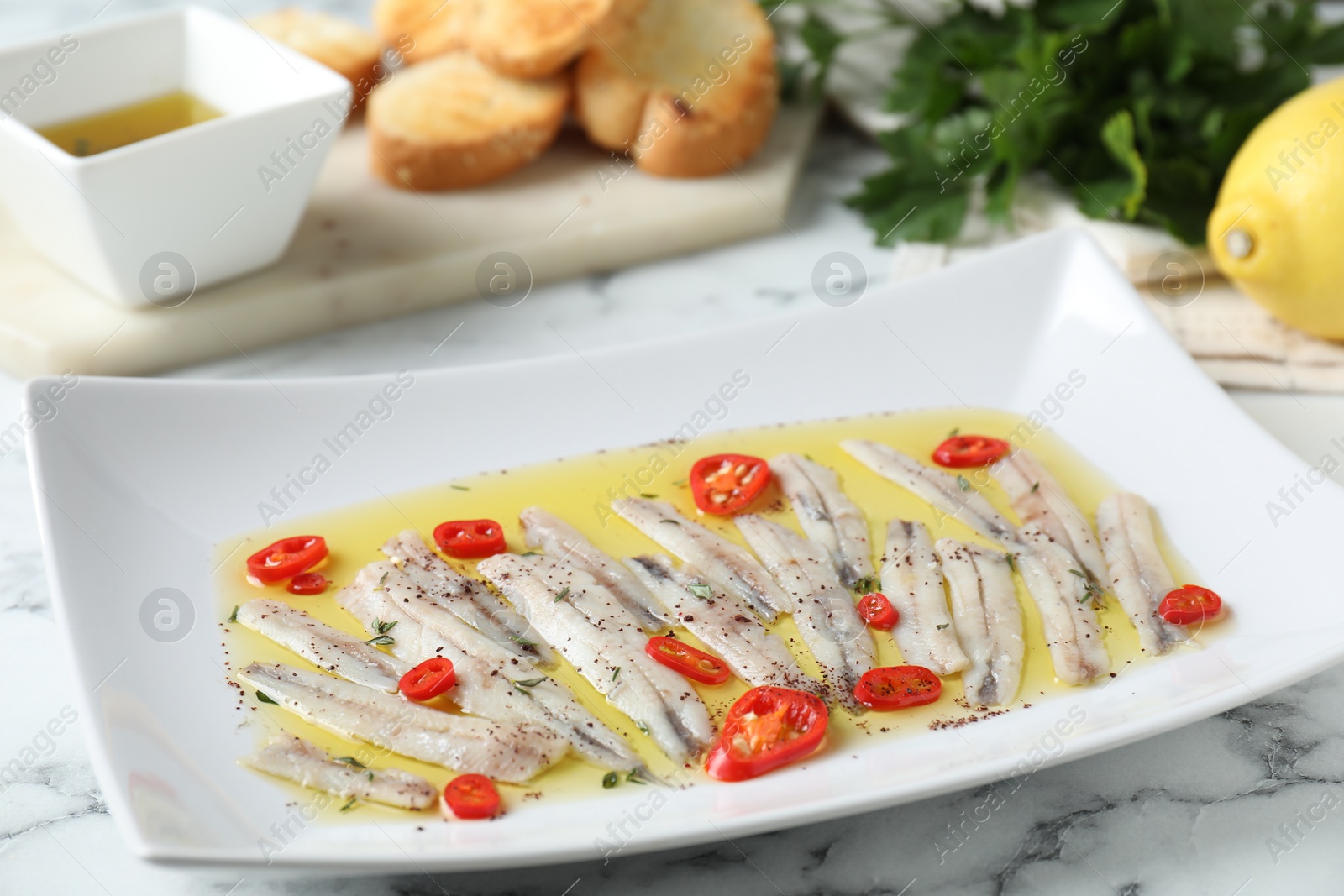 Photo of Tasty pickled anchovies with spices on white marble table, closeup