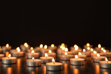 Many burning candles on table against dark background. Symbol of sorrow