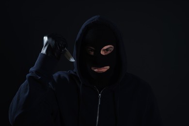 Photo of Man wearing knitted balaclava with knife on black background