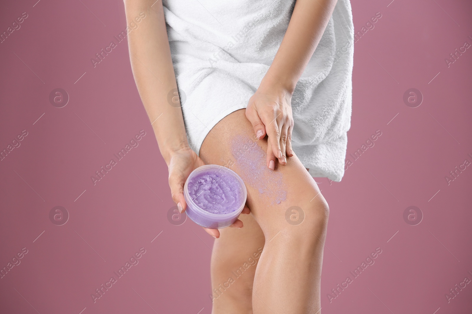 Photo of Young woman applying body scrub on leg against color background