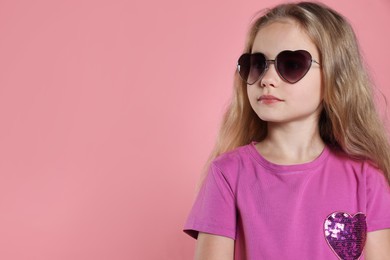 Photo of Girl wearing stylish sunglasses in shape of hearts on pink background. Space for text