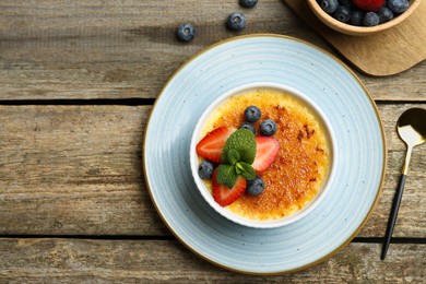 Photo of Delicious creme brulee with berries and mint in bowl served on wooden table, flat lay. Space for text