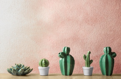 Photo of Decorative cacti on table near color wall, space for text. Interior decor