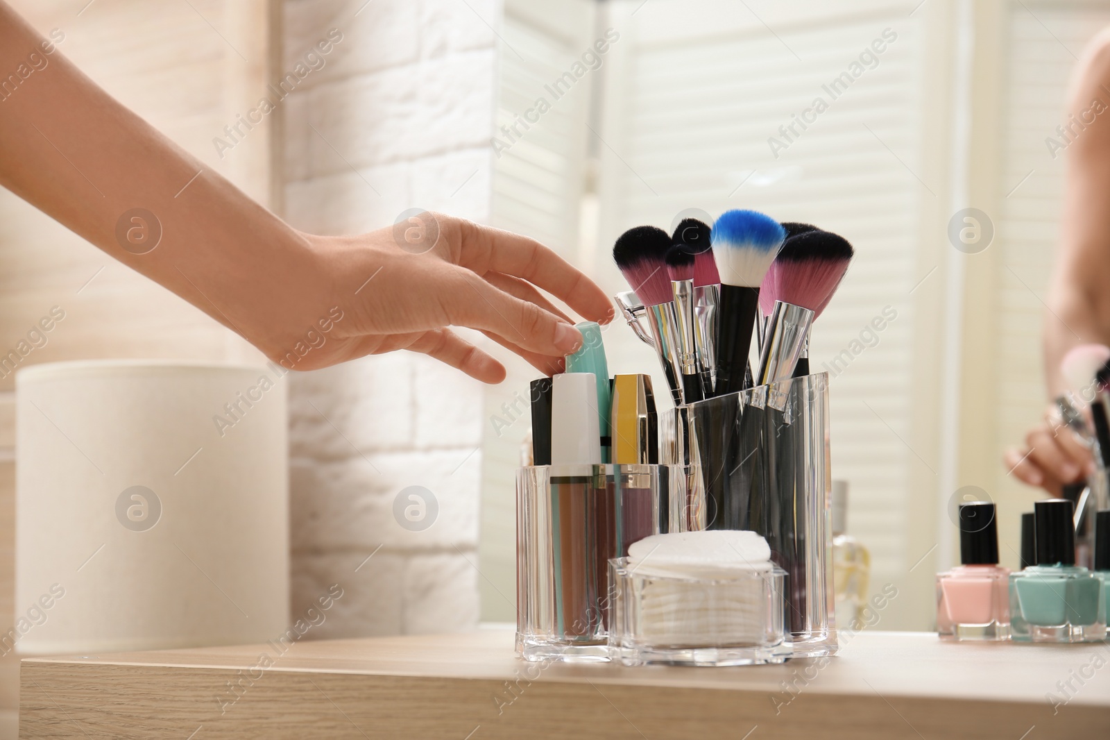 Photo of Woman taking mascara from organizer for makeup cosmetic products on table