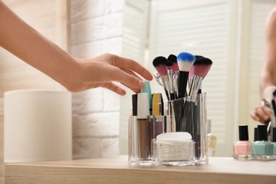 Photo of Woman taking mascara from organizer for makeup cosmetic products on table