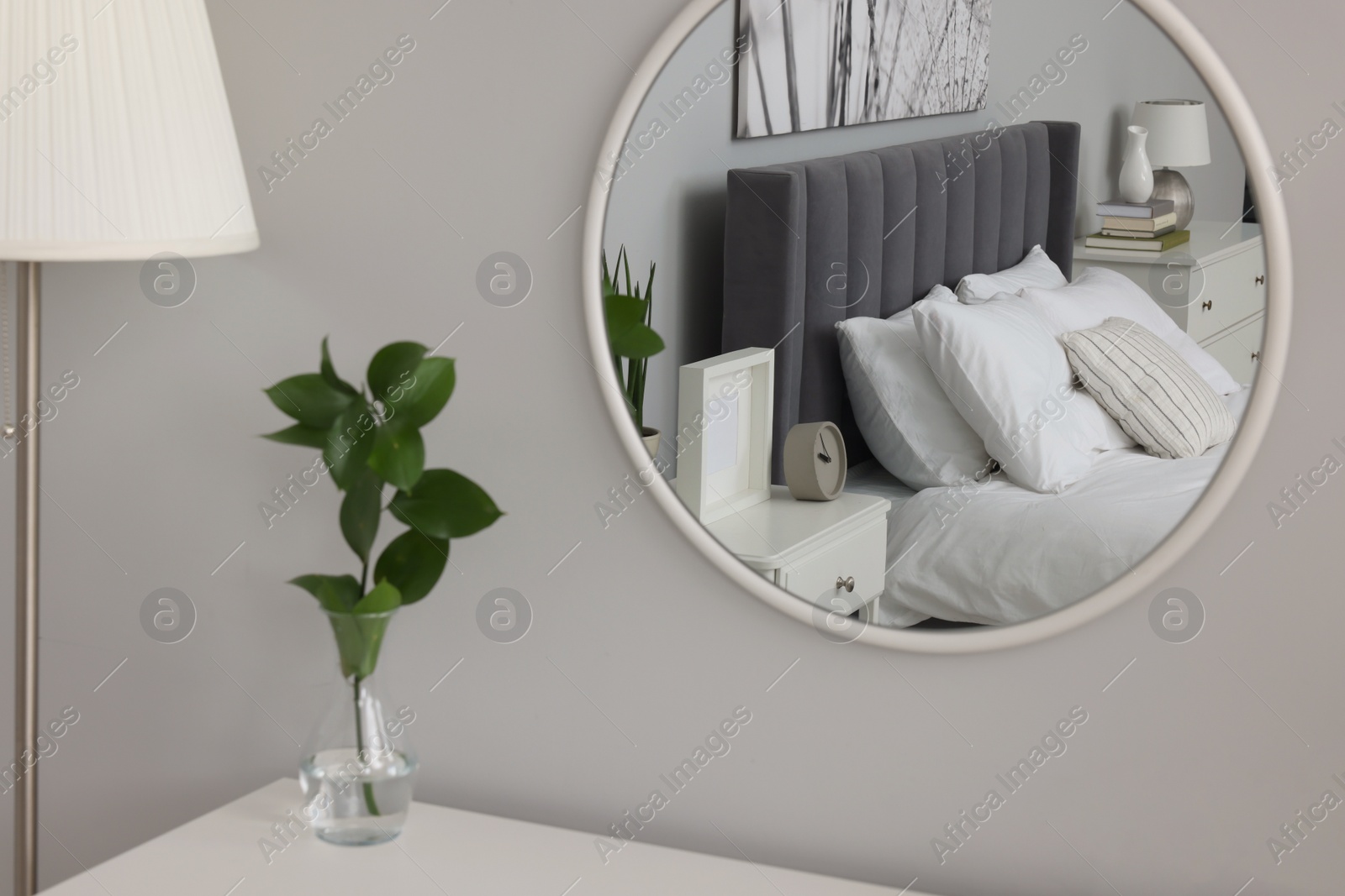 Photo of Reflection of large comfortable bed and bedside table in mirror on grey wall
