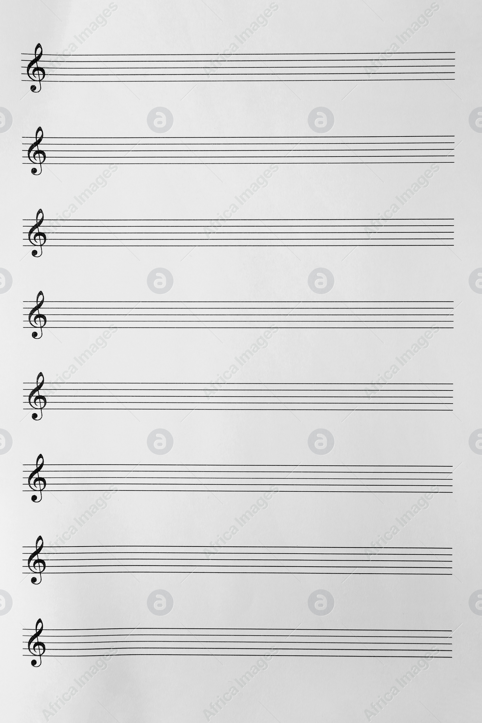 Photo of Sheet with empty staves for music notes and treble clef as background, top view