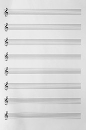 Photo of Sheet with empty staves for music notes and treble clef as background, top view