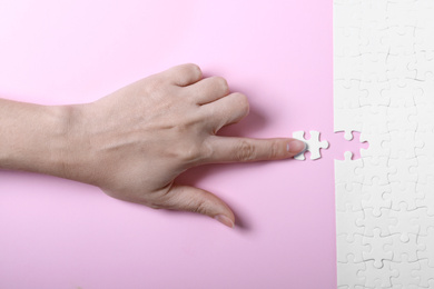 Photo of Woman putting last piece of white puzzle on pink background, closeup