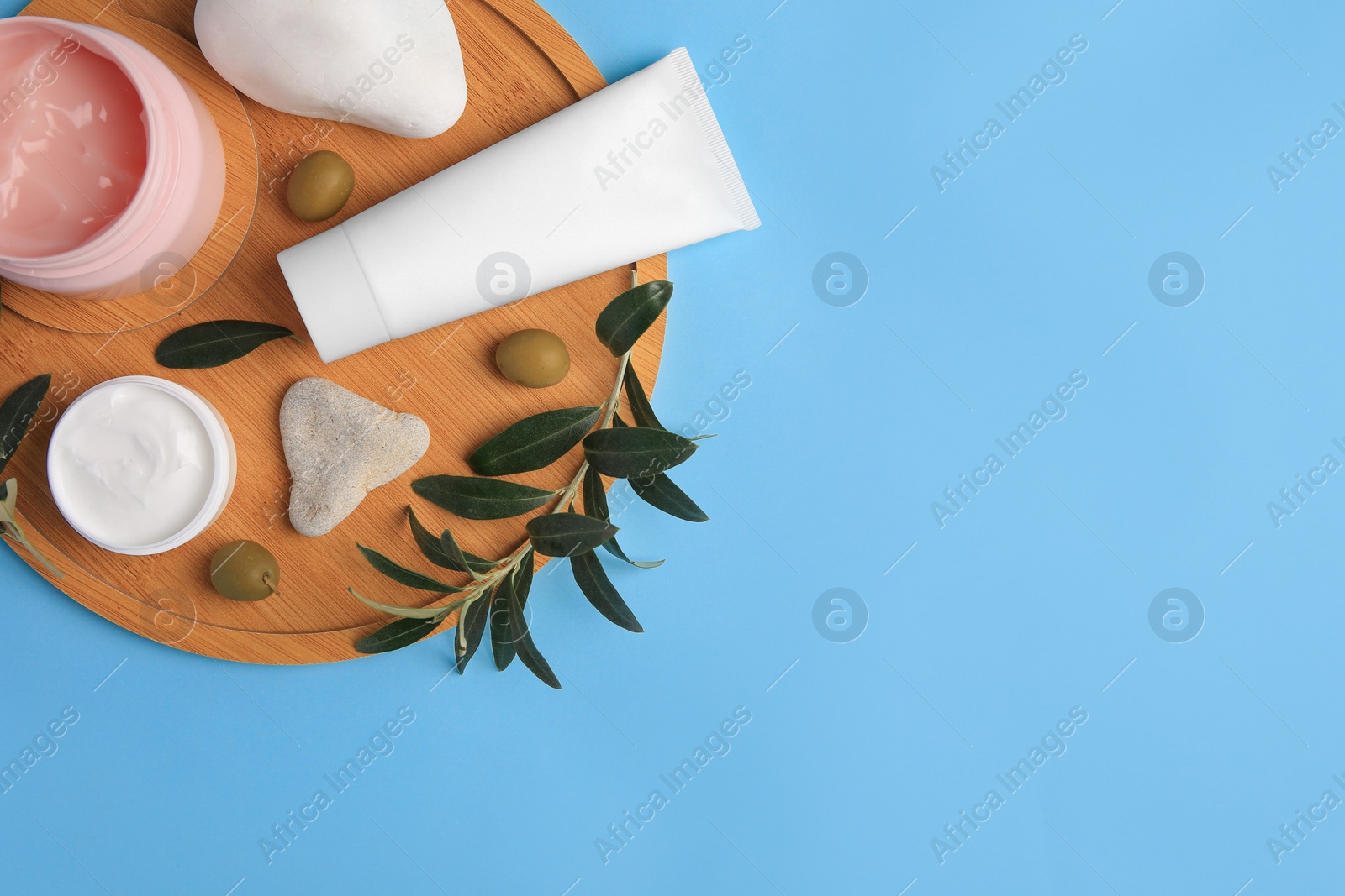 Photo of Different cosmetic products with olives and stones on light blue background, top view. Space for text