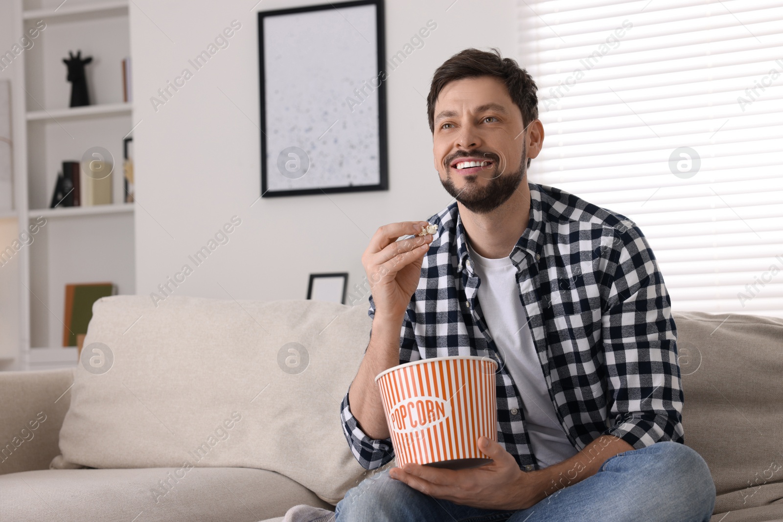 Photo of Happy man watching TV while eating popcorn on sofa at home