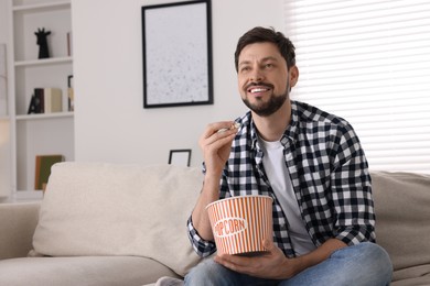 Happy man watching TV while eating popcorn on sofa at home