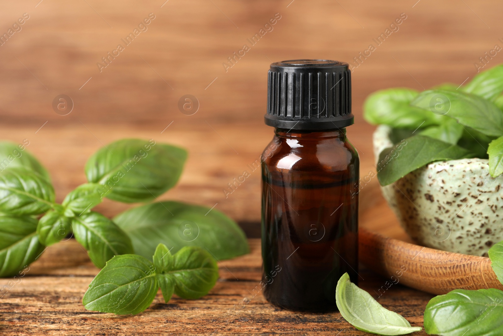 Photo of Glass bottle of basil essential oil and leaves on wooden table, space for text