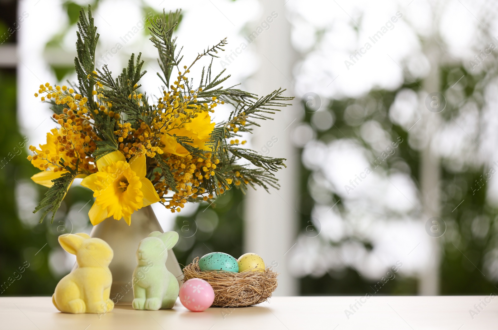 Photo of Festive composition with Easter eggs in decorative nest on table against blurred window, space for text