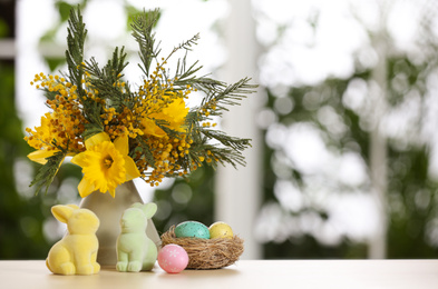 Photo of Festive composition with Easter eggs in decorative nest on table against blurred window, space for text