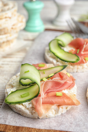 Puffed rice cakes with prosciutto and cucumber on wooden board, closeup