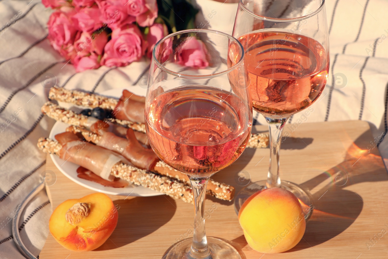 Photo of Glasses of delicious rose wine, flowers and food on white picnic blanket, closeup