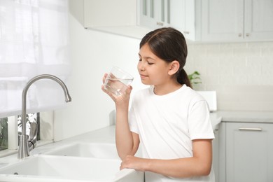 Photo of Girl drinking tap water from glass in kitchen