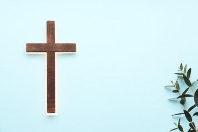 Shining cross and eucalyptus branches on light blue background, space for text. Religion of Christianity