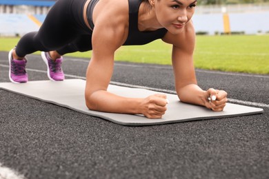 Photo of Young woman doing plank exercise at stadium, closeup