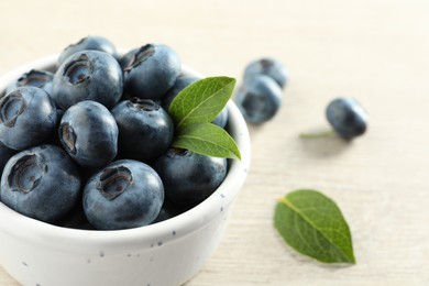 Photo of Bowl of fresh tasty blueberries with leaves on table, closeup. Space for text