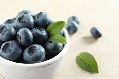 Bowl of fresh tasty blueberries with leaves on table, closeup. Space for text