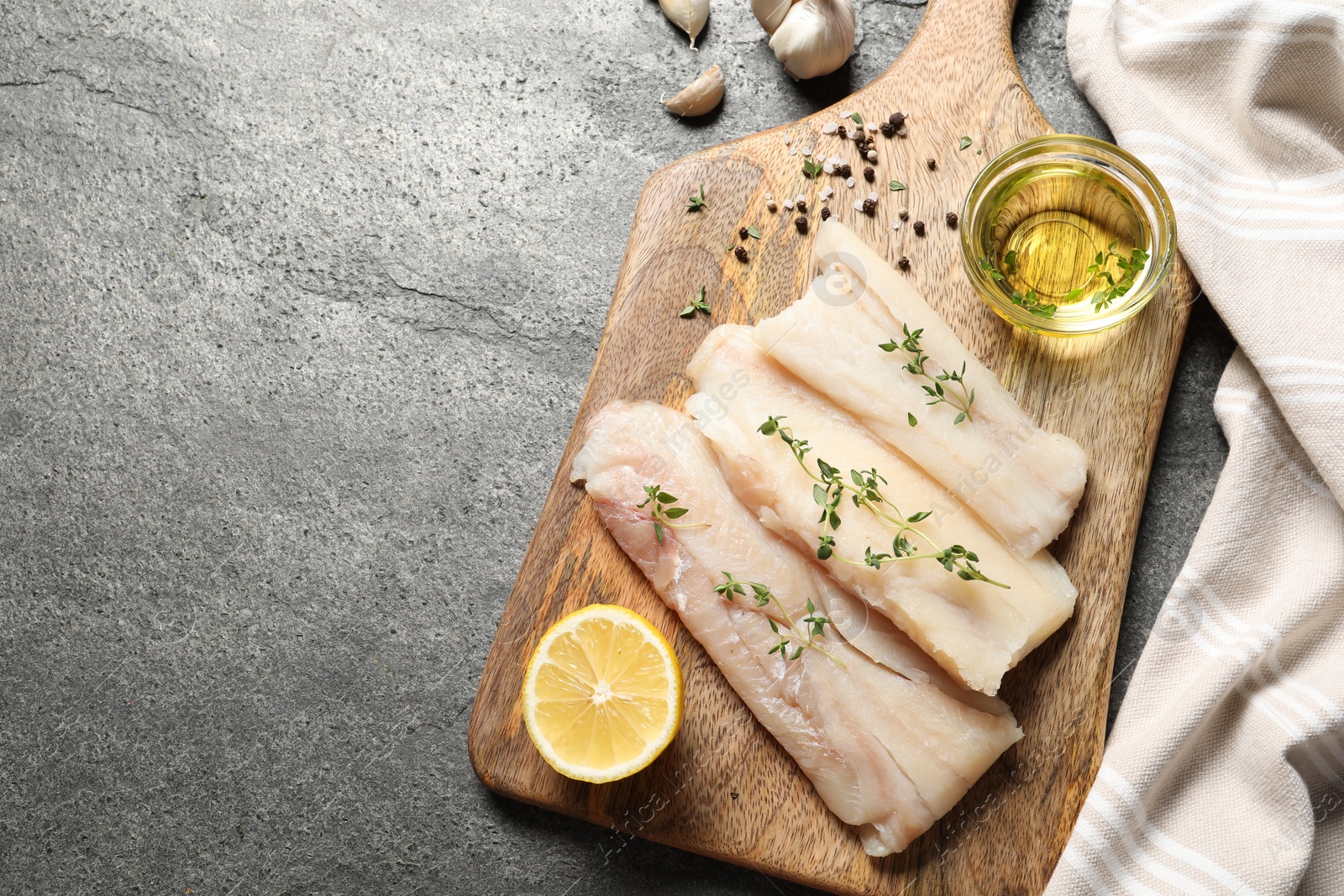 Photo of Raw cod fish, microgreens, oil, spices and lemon on grey textured table, top view. Space for text