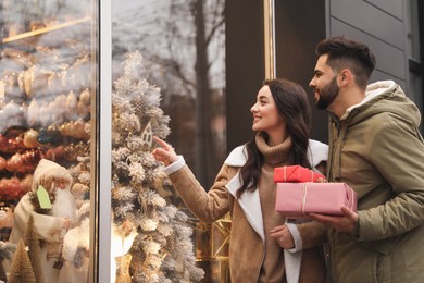 Lovely couple with presents near store decorated for Christmas outdoors