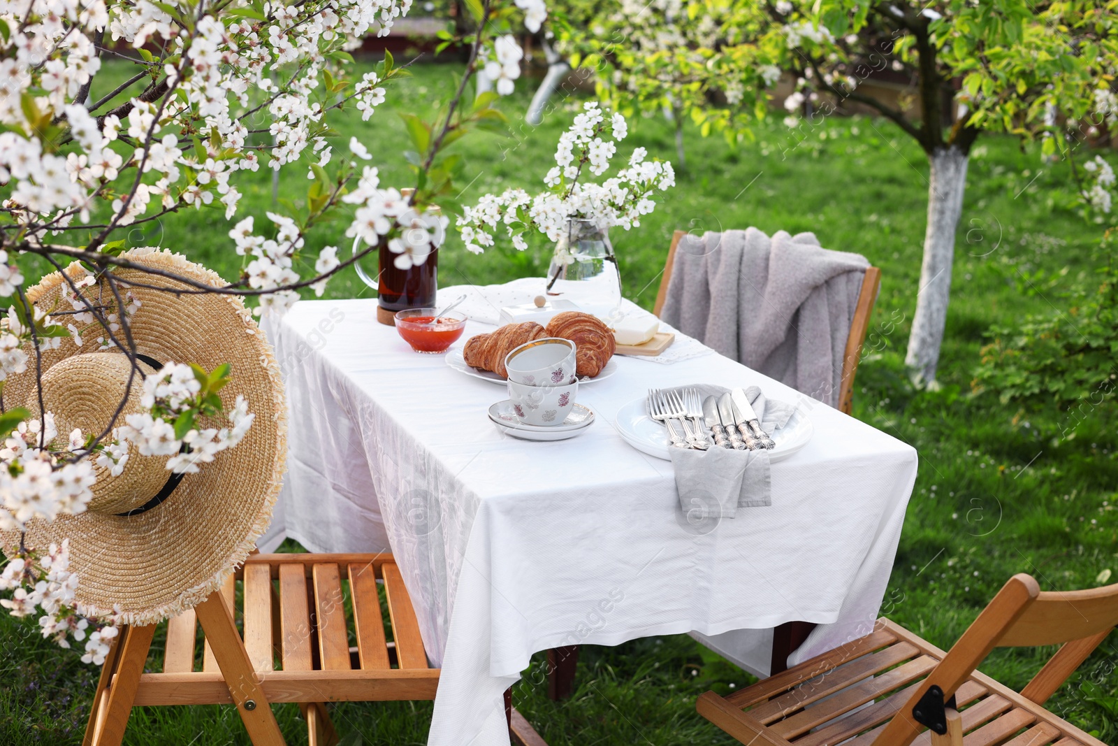 Photo of Stylish table setting with beautiful spring flowers, tea and croissants in garden