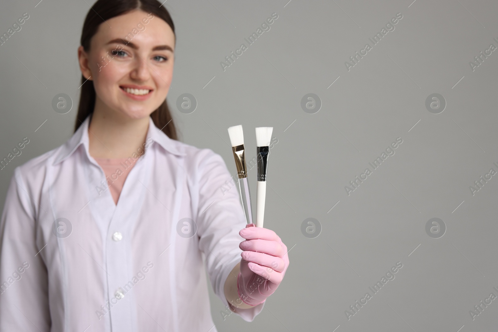 Photo of Cosmetologist with cosmetic brushes on grey background, selective focus. Space for text