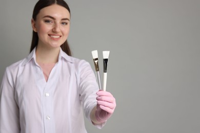 Cosmetologist with cosmetic brushes on grey background, selective focus. Space for text