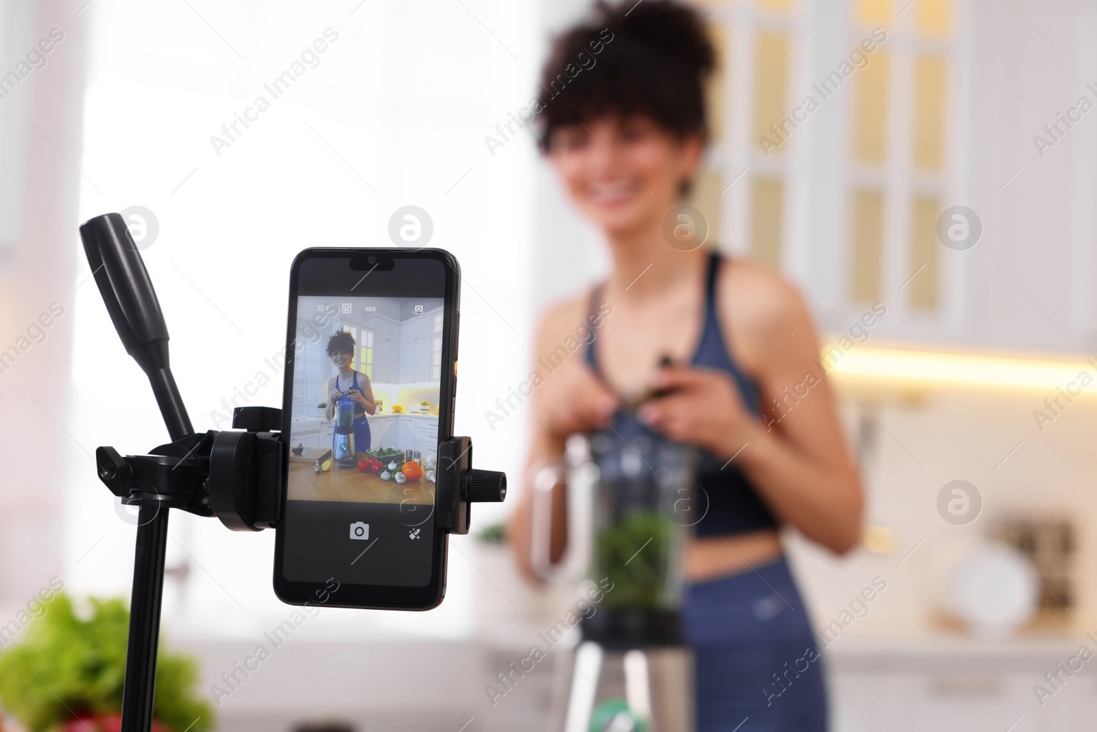 Photo of Food blogger recording video in kitchen, focus on smartphone