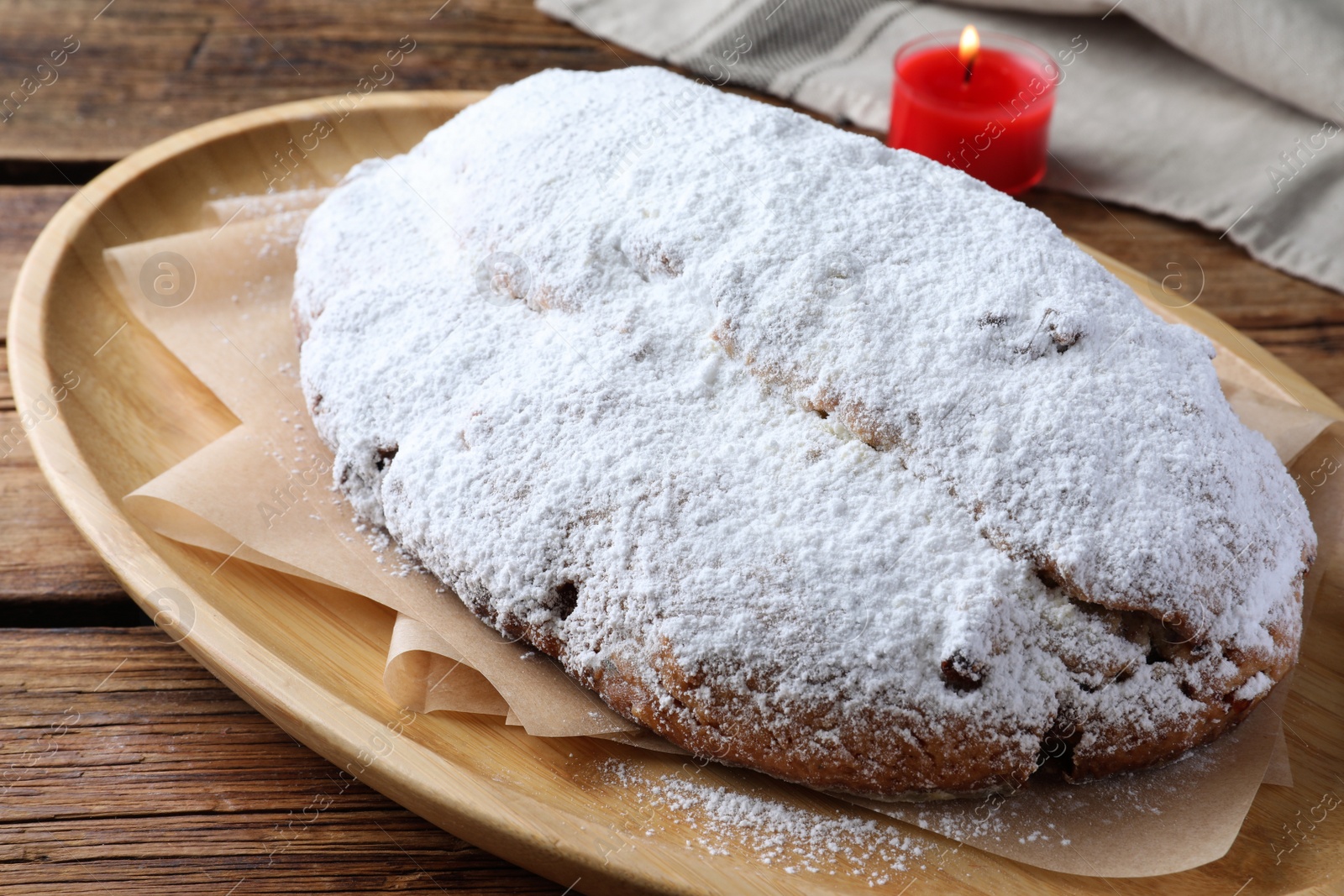 Photo of Wooden plate of delicious Stollen sprinkled with powdered sugar on table, closeup